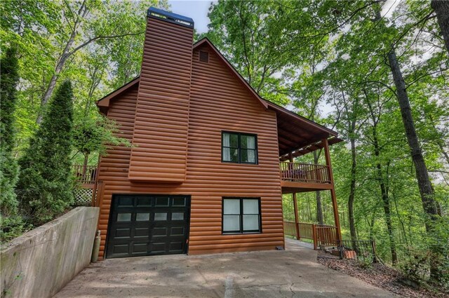 view of side of home with driveway, a chimney, faux log siding, a garage, and a balcony