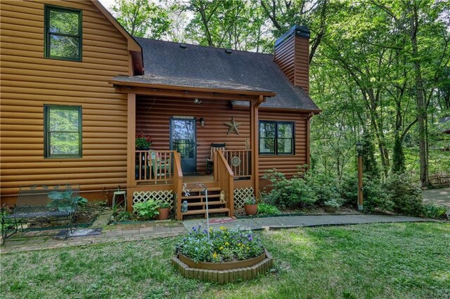 back of house with a lawn, a deck, a chimney, and a shingled roof