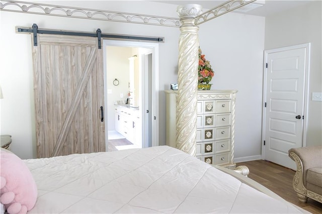 bedroom with connected bathroom, a barn door, and hardwood / wood-style floors