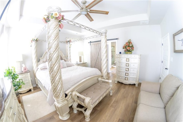 bedroom featuring ceiling fan, hardwood / wood-style floors, connected bathroom, a raised ceiling, and a barn door