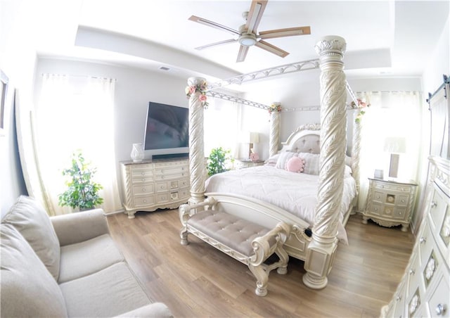 bedroom with ceiling fan, a barn door, a raised ceiling, and light hardwood / wood-style flooring