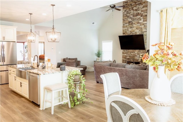 kitchen with hanging light fixtures, a center island with sink, stainless steel appliances, a fireplace, and light stone countertops