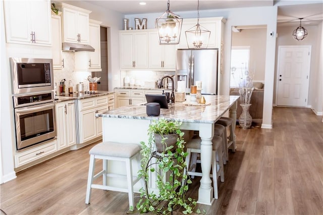 kitchen featuring a breakfast bar, light stone counters, appliances with stainless steel finishes, an island with sink, and pendant lighting