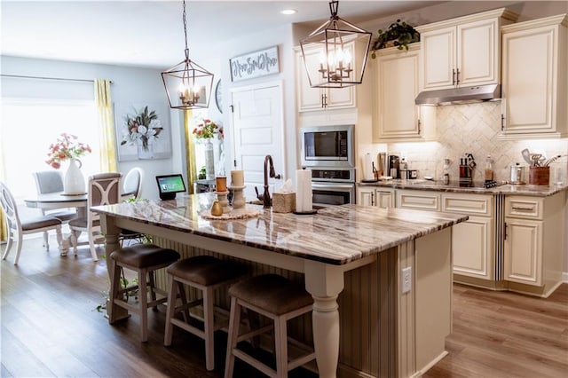 kitchen featuring stainless steel appliances, light stone countertops, hanging light fixtures, and a center island with sink