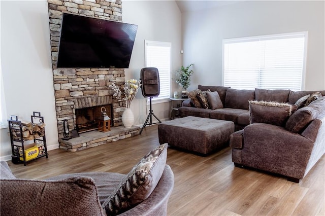 living room featuring a stone fireplace, lofted ceiling, and light wood-type flooring