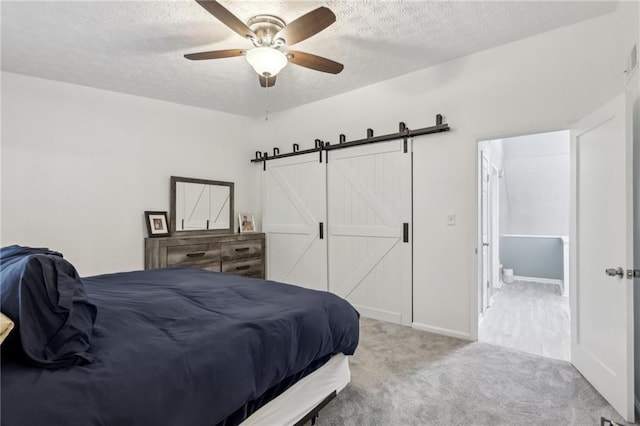 bedroom with ceiling fan, light colored carpet, a barn door, and a textured ceiling