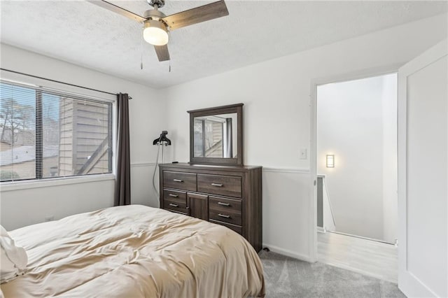 bedroom with ceiling fan, light colored carpet, and a textured ceiling