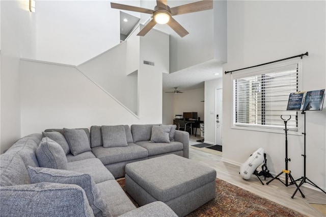 living room featuring a high ceiling, ceiling fan, and light wood-type flooring