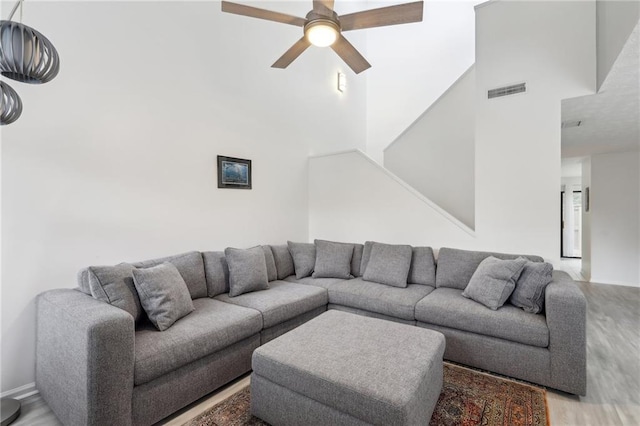 living room with ceiling fan, wood-type flooring, and a high ceiling