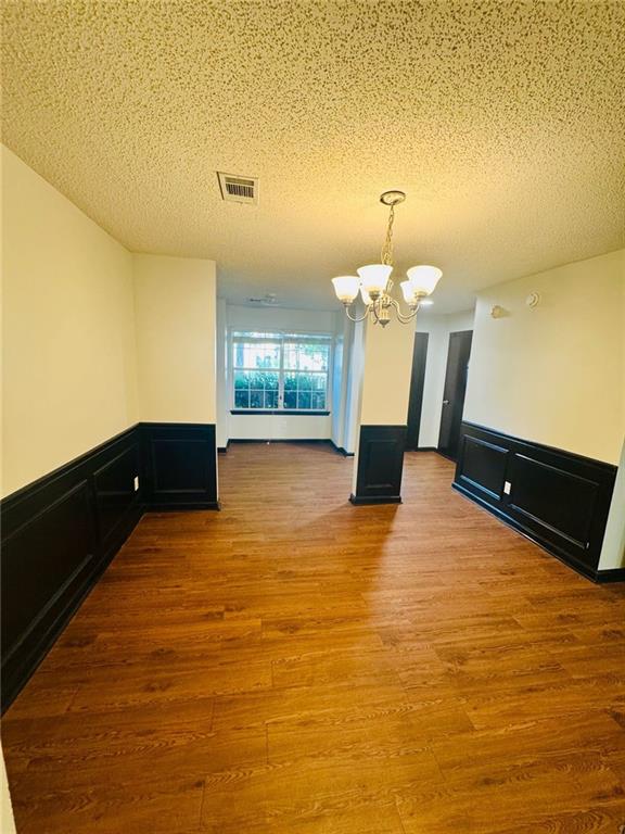 225 Colser Dr, Covington, GA 30016 - unfurnished room with a chandelier, a textured ceiling, wood finished floors, and a wainscoted wall