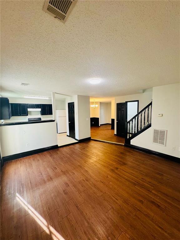 225 Colser Dr, Covington, GA 30016 - unfurnished living room with a textured ceiling, baseboards, wood-type flooring, and stairway