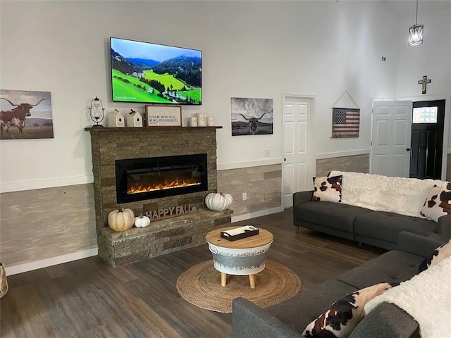 living room with a stone fireplace, a towering ceiling, and dark wood-type flooring