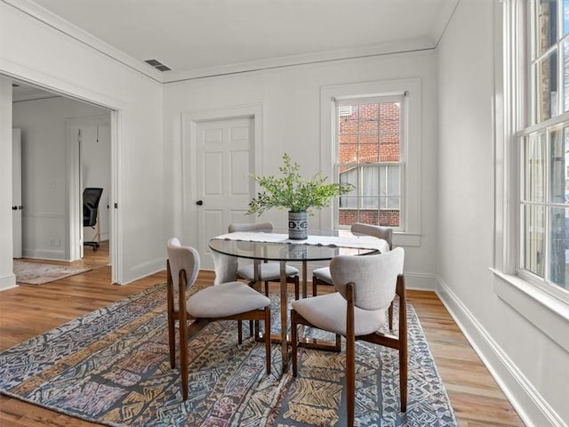 dining area featuring baseboards, light wood-style flooring, visible vents, and crown molding