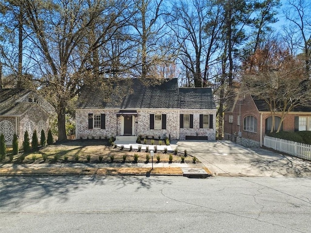 cape cod home with concrete driveway, brick siding, fence, and roof with shingles