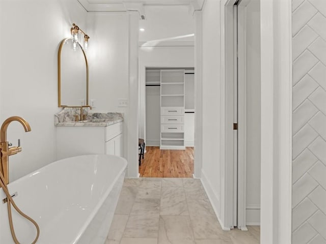 bathroom featuring marble finish floor, a freestanding tub, a walk in closet, and vanity