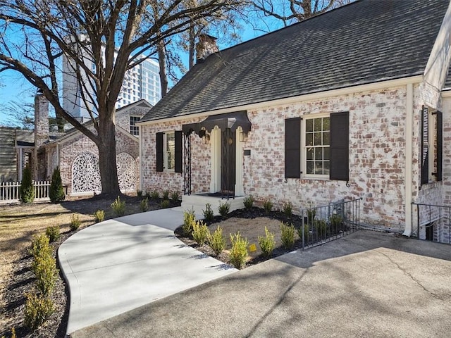 view of front facade featuring a shingled roof, a chimney, and fence