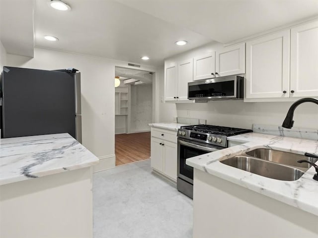 kitchen with light stone counters, recessed lighting, appliances with stainless steel finishes, white cabinetry, and a sink