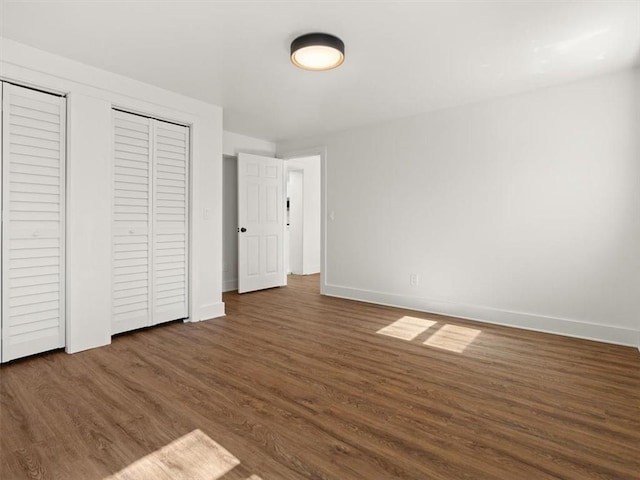 unfurnished bedroom featuring multiple closets, wood finished floors, and baseboards