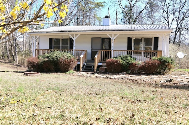 view of front of home with covered porch, a chimney, and metal roof