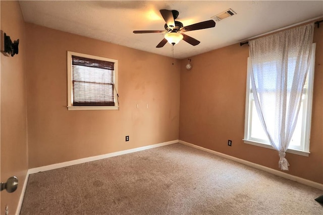 carpeted spare room featuring baseboards, visible vents, and ceiling fan