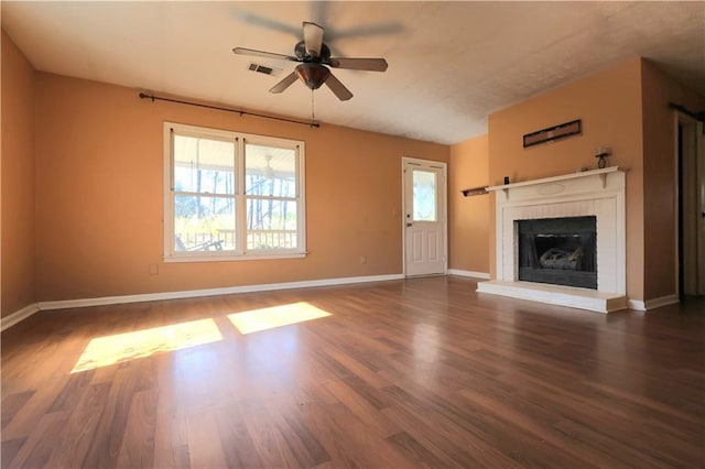 unfurnished living room with wood finished floors, visible vents, baseboards, a fireplace with raised hearth, and ceiling fan