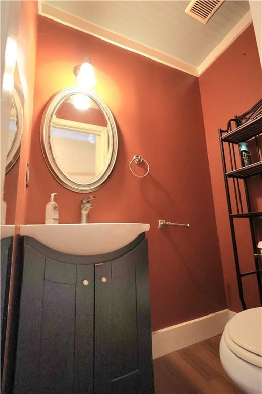 bathroom featuring visible vents, baseboards, toilet, wood finished floors, and vanity