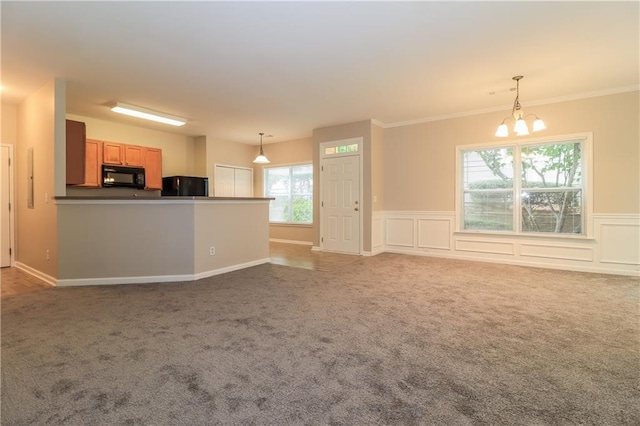 unfurnished living room featuring carpet flooring, a wealth of natural light, crown molding, and a notable chandelier