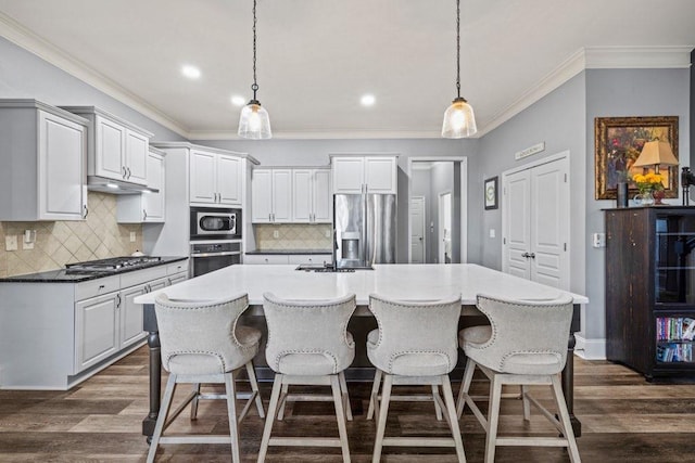 kitchen with decorative light fixtures, a center island with sink, decorative backsplash, appliances with stainless steel finishes, and dark hardwood / wood-style flooring