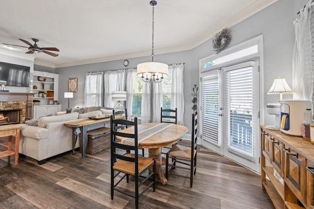 dining room featuring a fireplace, dark hardwood / wood-style flooring, crown molding, and ceiling fan with notable chandelier