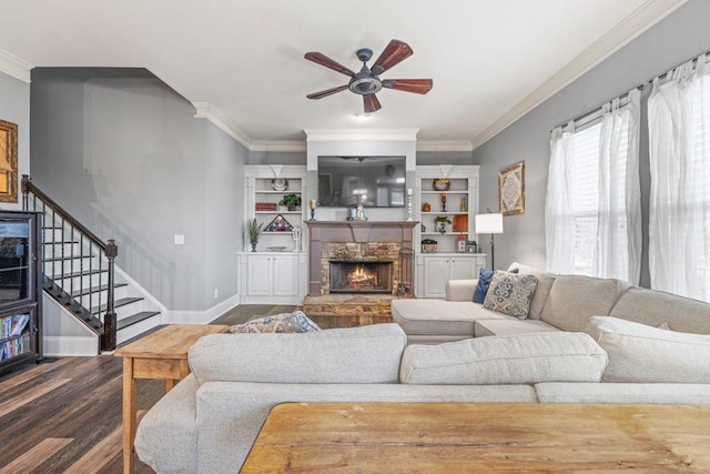 living room with ceiling fan, dark hardwood / wood-style floors, crown molding, and a stone fireplace