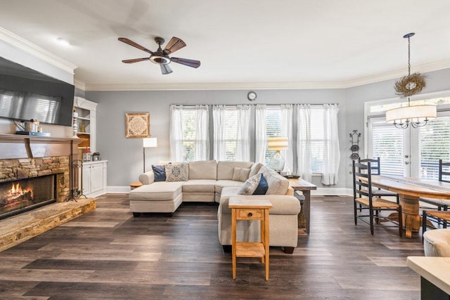 living room featuring a healthy amount of sunlight, a stone fireplace, ceiling fan with notable chandelier, and ornamental molding