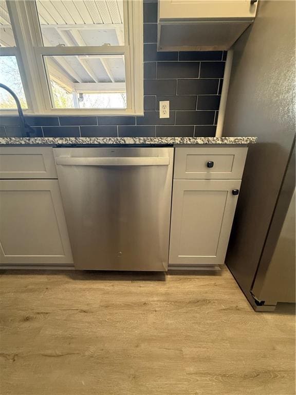 kitchen featuring stone counters, appliances with stainless steel finishes, light hardwood / wood-style floors, and decorative backsplash