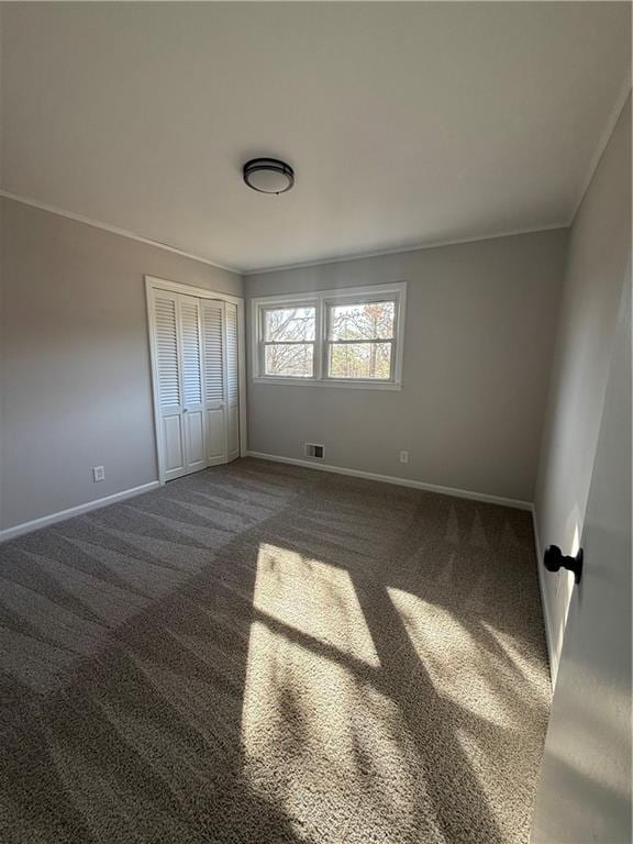 unfurnished bedroom with crown molding, dark carpet, and a closet