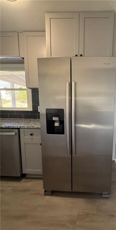 kitchen with appliances with stainless steel finishes, backsplash, light stone countertops, light hardwood / wood-style floors, and white cabinets