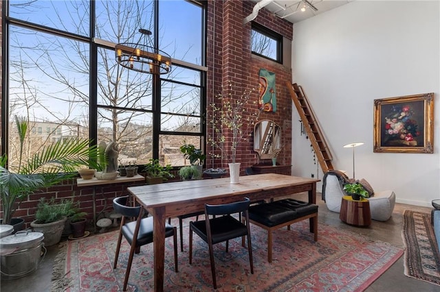 dining space featuring a chandelier, a high ceiling, brick wall, and finished concrete flooring