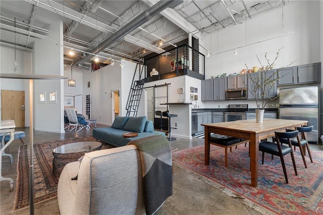 living area with baseboards, concrete flooring, and a towering ceiling