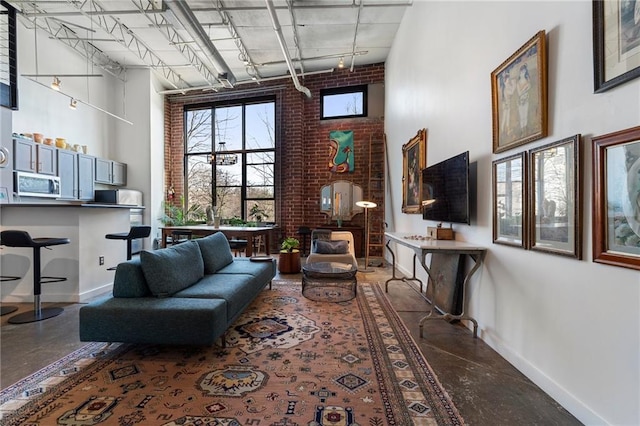 living area with track lighting, brick wall, concrete floors, and a towering ceiling