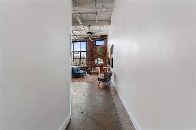 hallway featuring brick wall, concrete floors, and baseboards