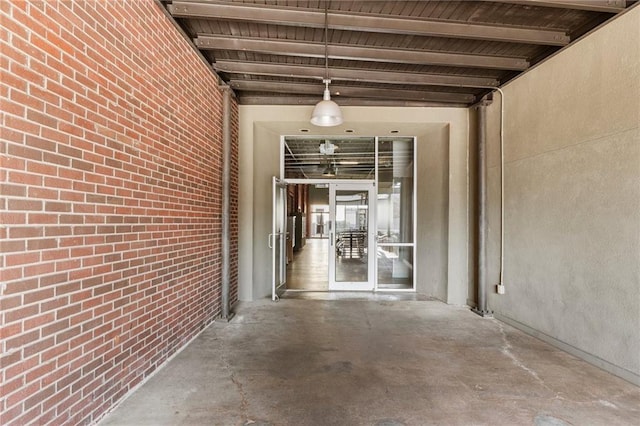 hall featuring beamed ceiling, concrete flooring, and brick wall