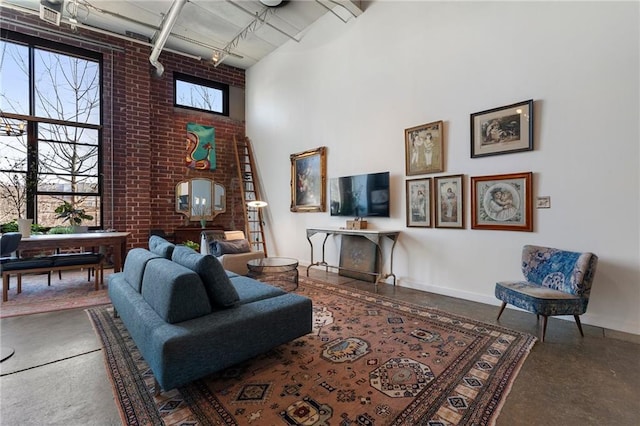 living room featuring rail lighting, a high ceiling, finished concrete flooring, and brick wall