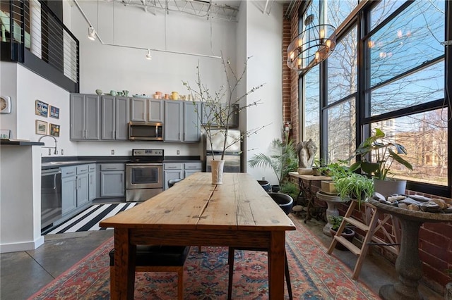 kitchen with dark countertops, gray cabinetry, a high ceiling, stainless steel appliances, and a sink