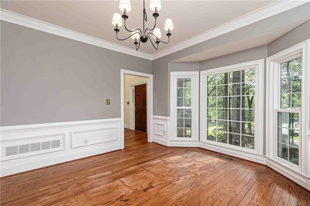 unfurnished dining area with a chandelier, wood finished floors, ornamental molding, and wainscoting