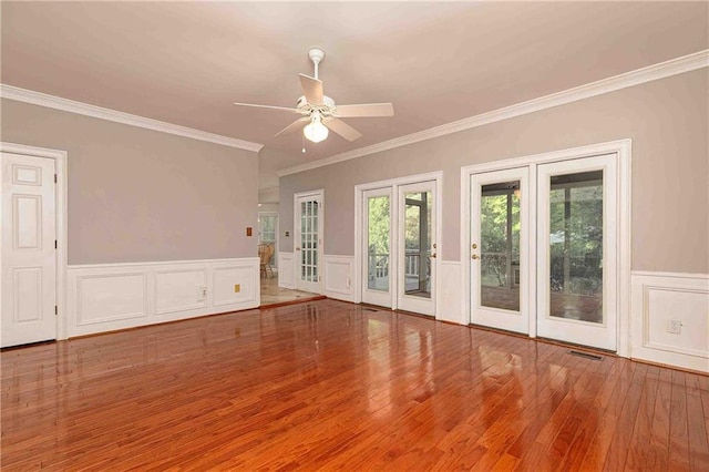 empty room featuring ornamental molding, ceiling fan, wainscoting, wood finished floors, and a decorative wall