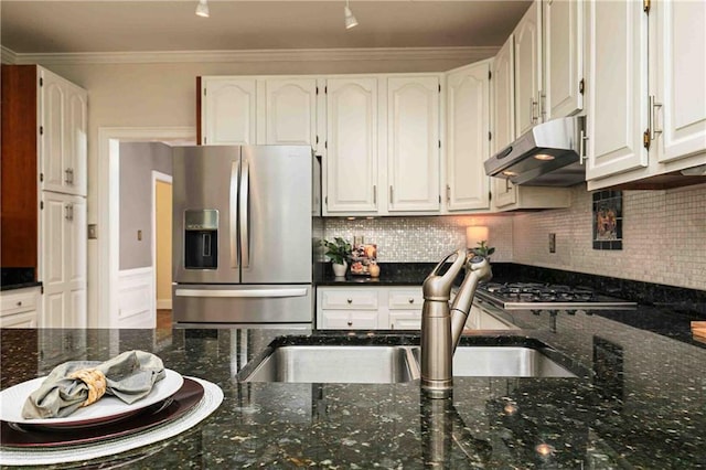 kitchen with stainless steel appliances, under cabinet range hood, a sink, dark stone counters, and white cabinetry