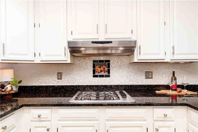 kitchen featuring stainless steel gas stovetop, under cabinet range hood, white cabinetry, backsplash, and dark stone counters