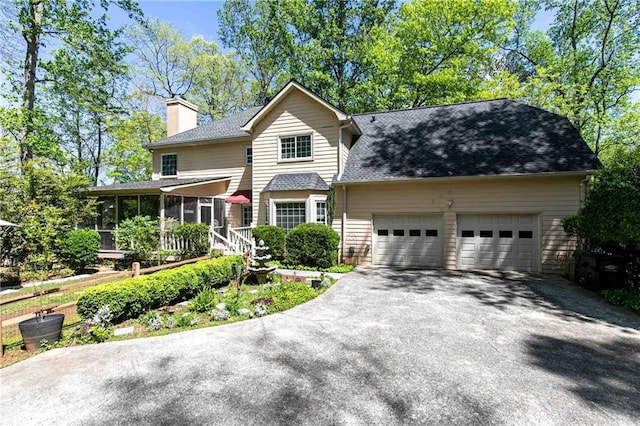traditional-style house featuring a sunroom, asphalt driveway, an attached garage, a chimney, and a shingled roof