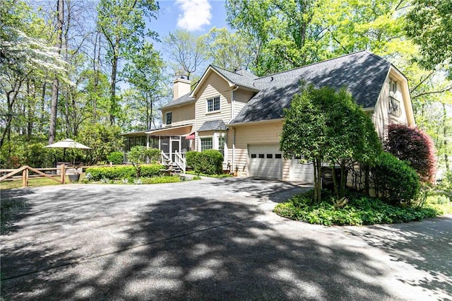 view of front of property featuring a sunroom, an attached garage, driveway, a chimney, and a shingled roof