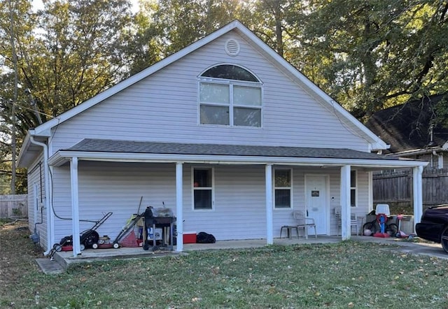 view of front of home featuring a front lawn, a porch, fence, and a shingled roof