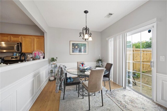 212 Regent Sq, Woodstock, GA 30188 - dining space with visible vents, a decorative wall, a wainscoted wall, light wood-style flooring, and a notable chandelier