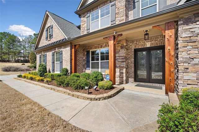 view of exterior entry featuring brick siding, stone siding, and french doors